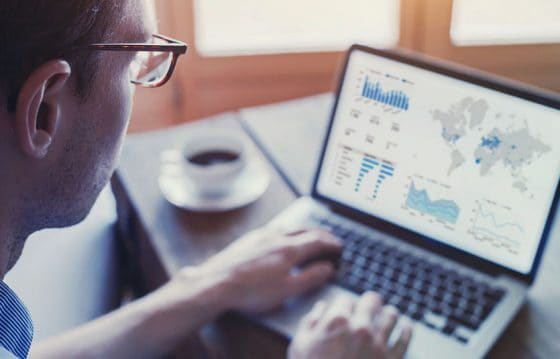 A business analysts looks over statistics on his laptop and looks for trends on graphs.