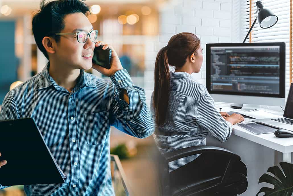 a man with laptop in hand and talking on phone with a girl in background coding something on desktop